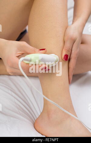 Mädchen Epilates ihr Bein mit einem Epilierer auf dem Bett Stockfoto