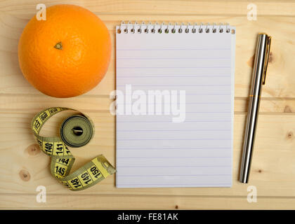 Notebook mit Orangenfrucht und Zentimeter auf Holztisch Stockfoto