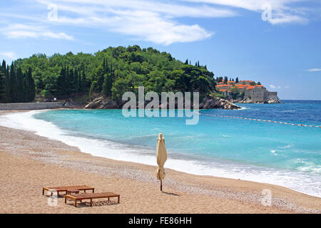 Leerer Strand mit zwei Stühlen und Sonnenschirm in der Nähe von Sveti Stafan Insel, Montenegro Stockfoto