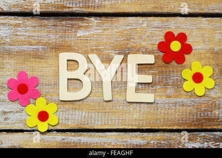 Wort-Bye mit Holzbuchstaben auf rustikale Oberfläche und bunte Blumen geschrieben Stockfoto