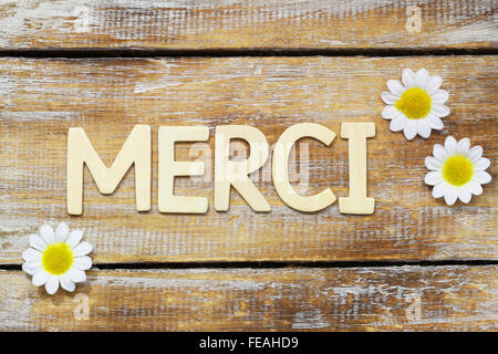 Merci (Danke in französischer Sprache) mit Holzbuchstaben auf rustikale Oberfläche und White Daisy Blumen geschrieben Stockfoto