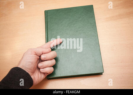 Männliche Hand mit Zeigefinger zeigt auf Buch mit leeren dunklen grünen Lederbezug Handauflegen Schreibtisch aus Holz Stockfoto