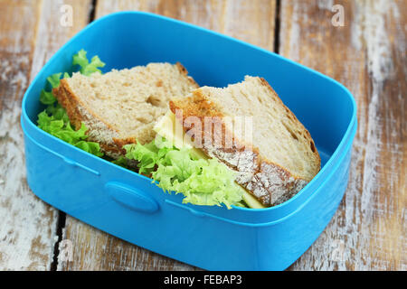 Rustikales Brot Brötchen mit Käse und Salat in Lunchpaket auf Holzuntergrund Stockfoto