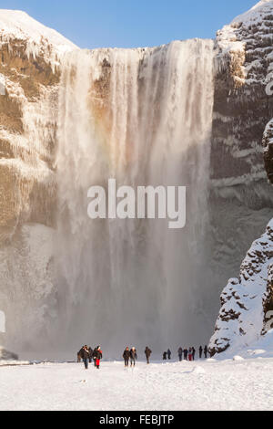 Große Gruppe von Touristen im Skogafoss Wasserfall, Südisland im Januar mit gefrorenen Eiszapfen Stockfoto