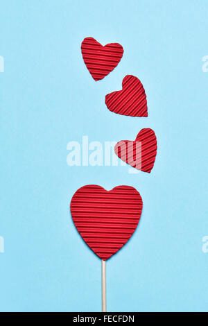 einige Herzen gemacht mit rote gewellte Pappe, eines davon gestapelt in einem Stick wie einen Lutscher, auf blauem Grund Stockfoto