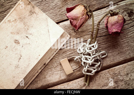 Altes Buch und zwei trockene verkettete Rosen auf dem hölzernen Hintergrund Stockfoto