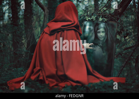 Geheimnisvolle rote Kapuze Frau vor einem magischen Spiegel. Dark fantasy Stockfoto