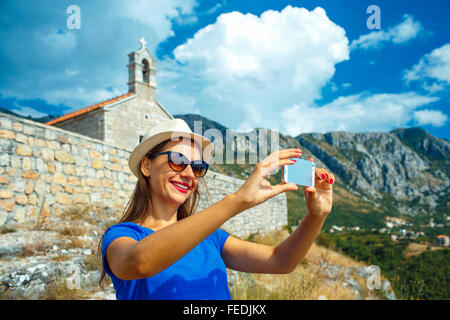 Mädchen in den Hut Selfie, indem das Smartphone auf dem Hintergrund der Kirche in den Bergen, Montenegro, Balkan Stockfoto
