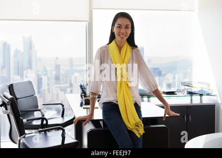 Multiethnische chinesische Hispanic weibliche Jungunternehmer stützte sich auf Tabelle in ein modernes Bürogebäude mit Blick auf die Stadt. Sie Stockfoto