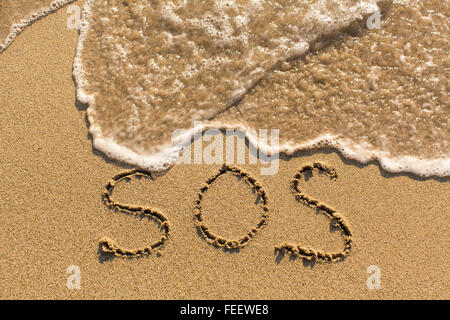 SOS - Wort auf dem Sandstrand mit der weichen Welle gezogen. Stockfoto