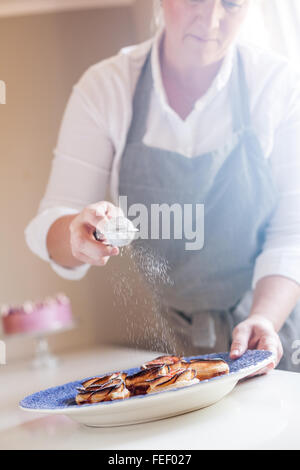 Kaukasische Frau Sichten Puderzucker über Brötchen Stockfoto