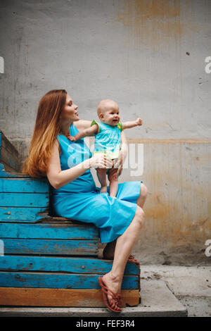 Cute 1 Jahr Baby stehend auf Mutters Knie. Familie Kleidungsstil mit blauen Farben. Selektiven Fokus auf Mutter. Stockfoto