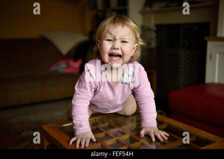 Ein unglücklich achtzehn Monate altes Baby mit einer Temperatur knelling einem Beistelltisch in ihrem Haus weint und sucht unglücklich. Stockfoto