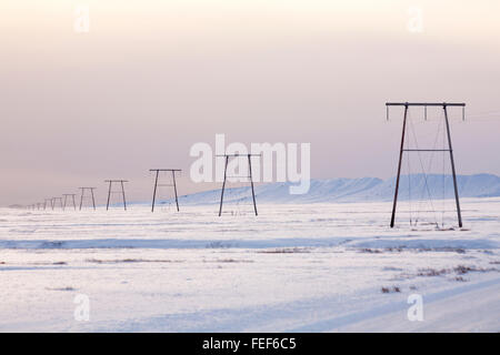 Die Strommeihe der Pylone ging im Januar in Island in die Ferne zurück - minimalistische Landschaft landschaftlich reizvoll - Schnee-Minimalismus Stockfoto