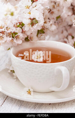 Tasse Tee auf einem weißen Hintergrund aus Holz. Die Zweige der Kirsche blüht. Selektiven Fokus Stockfoto