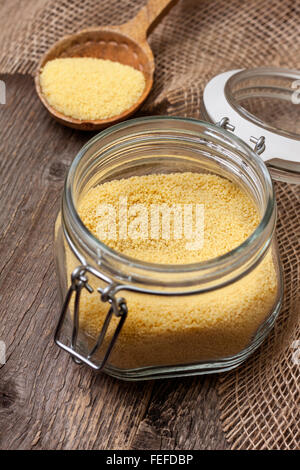 Couscous in ein Glas auf einem hölzernen Hintergrund, Holzlöffel mit couscous Stockfoto