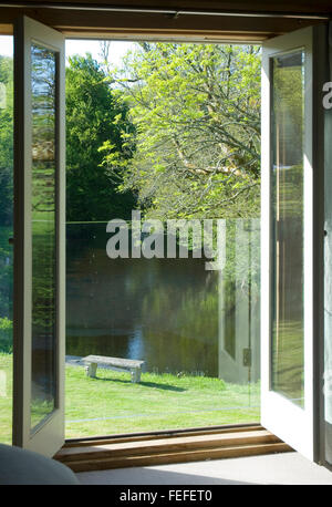 Glastüren mit Blick auf Fluss, öffnen verglaste Türen, neue Build Sonnenlicht und Schatten, Flussufer mit Sitzbank, Frühling. Stockfoto