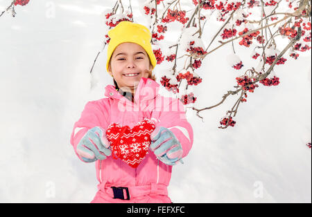 Kleines Mädchen hält Herz gemacht aus Textil mit Schnee im Hintergrund Stockfoto