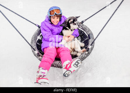 Glückliche kleine Mädchen sitzen auf der Schaukel mit husky Welpen Hund im winter Stockfoto