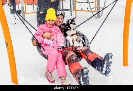 Mann sitzt auf der Schaukel mit husky Welpen Hund und seiner Tochter in der Winterzeit Stockfoto