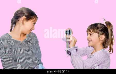 Kleines Mädchen fotografieren ihrer Schwester mit Kamera isoliert auf rosa Stockfoto