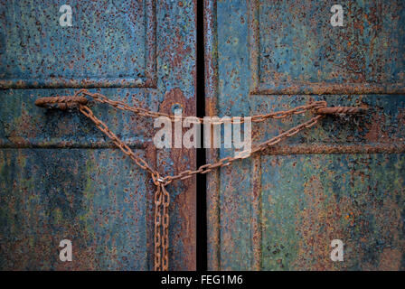Eine stark verwitterte Stahltüren ist angekettet und verschloss.   He Türen geknackt einen kleinen Splitter im Inneren frei. Stockfoto