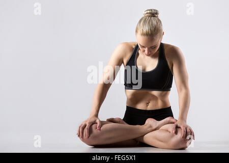 Porträt von sportlich schöne junge Frau, Yoga zu praktizieren, sitzen mit gekreuzten Beinen, bei der Durchführung von Padmasana, Lotus-Haltung, Stockfoto