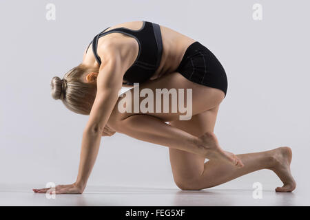 Sportlich schöne junge Frau Yoga zu praktizieren, dabei Knie, Stirn Übung, Eka Pada Marjariasana, arbeiten in schwarzer Stockfoto
