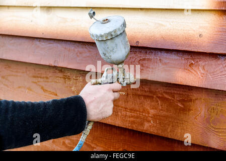 Man malt Holzhaus mit Spritzpistole Stockfoto