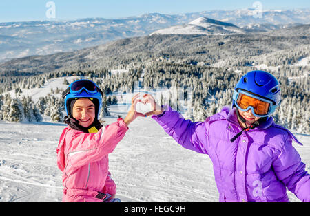 Zwei kleine Mädchen machen Herz mit ihren Händen im Schnee Stockfoto