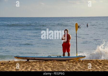 Ein Surf-Ski-Board-Fahrer steht in seinen Boardshorts am Collaroy Beach in Sydney und blickt auf das Wasser Stockfoto