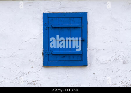 Horizontale Vorderansicht von blue Window mit geschlossenen hölzerne Blind auf einer weißen strukturierte Gebäudewand Stockfoto