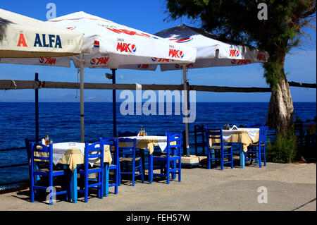 Kreta, Rethymnon, Straße Restaurant mit Blick auf das Meer, blaue Stühle, Tische und Sonnenschirme Stockfoto