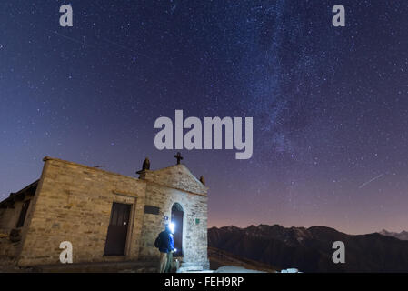 Die Milchstraße und den Sternenhimmel von hoch oben in den Alpen mit malerischen Berglandschaft. Menschen stehen neben einer kleinen Kapelle Stockfoto