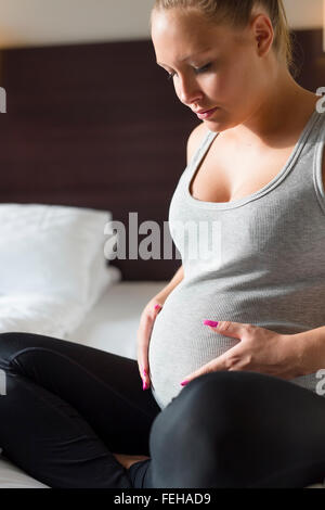 Schwangere Frau sitzt auf Bett mit der Hand am Bauch Stockfoto