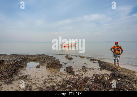 Ein Mann betrachtet sein Boot vor Anker in der Nähe der vulkanischen Vorland Orango Island in der Bijagos-Archipel, Guinea Bissau Stockfoto