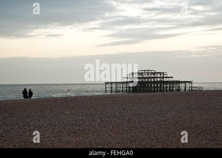 Blick auf Brighton Beach mit West Pier Ruinen und paar in Ferne in der Abenddämmerung. Stockfoto