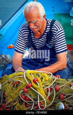 Ein älterer Wetter geschlagen Fischer trägt ein nautisches blau & weißen Hemd unter Overall auf Boot arbeitet auf der Suche nach Fisch im Netz Stockfoto