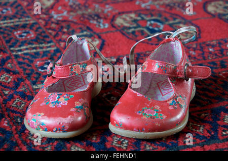 Ein gut getragen paar kleinen Mädchens leuchtend roten Schuhen auf einen Teppich gelegt. Stockfoto