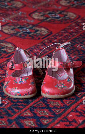 Ein gut getragen paar kleinen Mädchens leuchtend roten Schuhen auf einen Teppich gelegt. Stockfoto