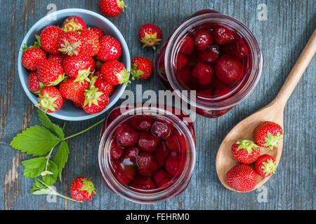 Glasgläser mit hausgemachten Erdbeere Konserve und frischen Erdbeeren in Schüssel von oben auf blauem rustikale Holz Hintergrund Stockfoto