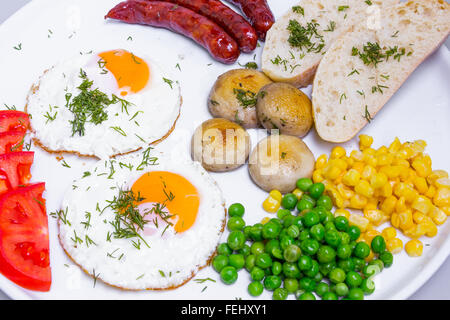 Reichhaltiges Frühstück mit Rührei, Würstchen und Gemüse in großen weißen Teller Stockfoto