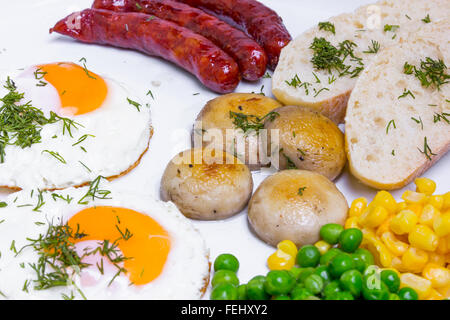 Reichhaltiges Frühstück mit Rührei, Würstchen und Gemüse in großen weißen Teller Stockfoto