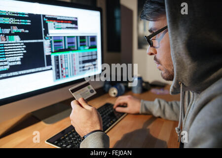 Junge Hacker konzentriert in Gläser stehlen Geld von verschiedenen Kreditkarten im dunklen Raum sitzen Stockfoto