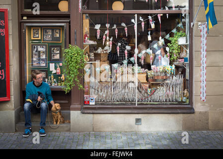 Junger Mann, sitzend mit Hund wartet in einer gepflasterten Straße in der Altstadt in einem der ältesten Süßigkeiten Geschäfte von Stockholm, Schweden Stockfoto