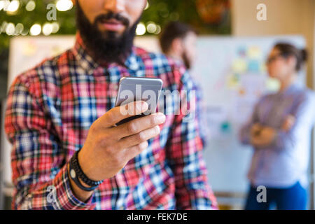 Beschnitten, Afro amerikanische Menschenbild mit Smartphone im Büro mit Kollegen im Hintergrund Stockfoto