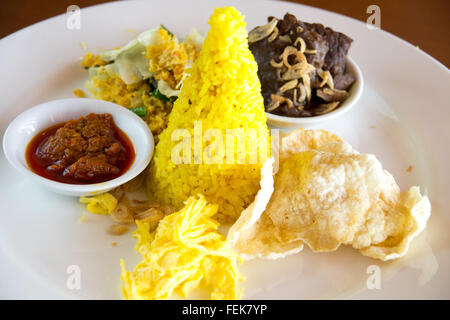 Nasi Kuning indonesischen gelber Reis mit geschmortem Rindfleisch serviert geschreddert Ei, Gemüse, Kokosnuss-Salat, hausgemachte Sambal und a Stockfoto