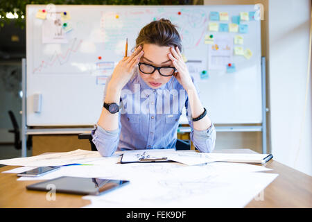 Erschöpfte junge Frau Modedesigner im Büro sitzen und Skizzen Stockfoto