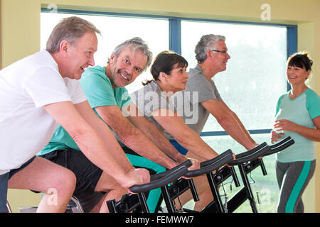 Eine Gruppe von Senioren, die mit Hilfe der Spinning-Bikes in der Turnhalle Stockfoto