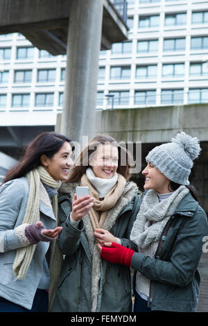Drei junge Frauen in der Stadt, etwas auf einem Smartphone betrachten. Stockfoto